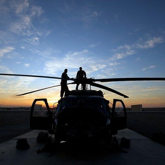 Two warfighters on top of a helicopter checking out the rotors at sunset
