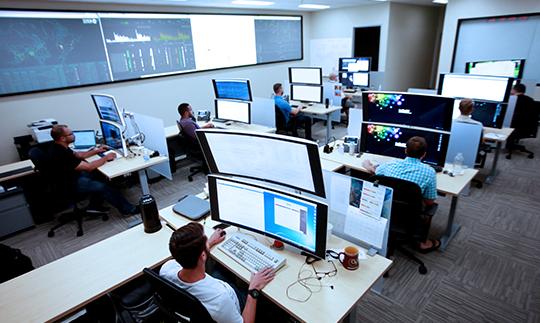 Viasat employees working at desks with 2 large, stacked monitors at a cybersecurity operations center